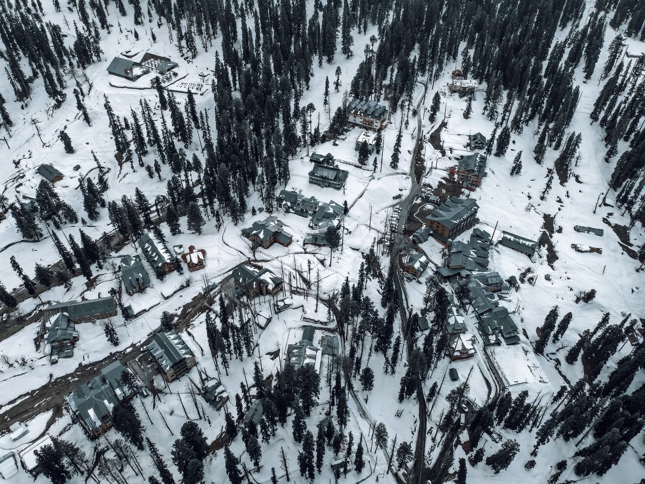 Snow-covered aerial view of Gulmarg, showcasing buildings and pine trees in winter.