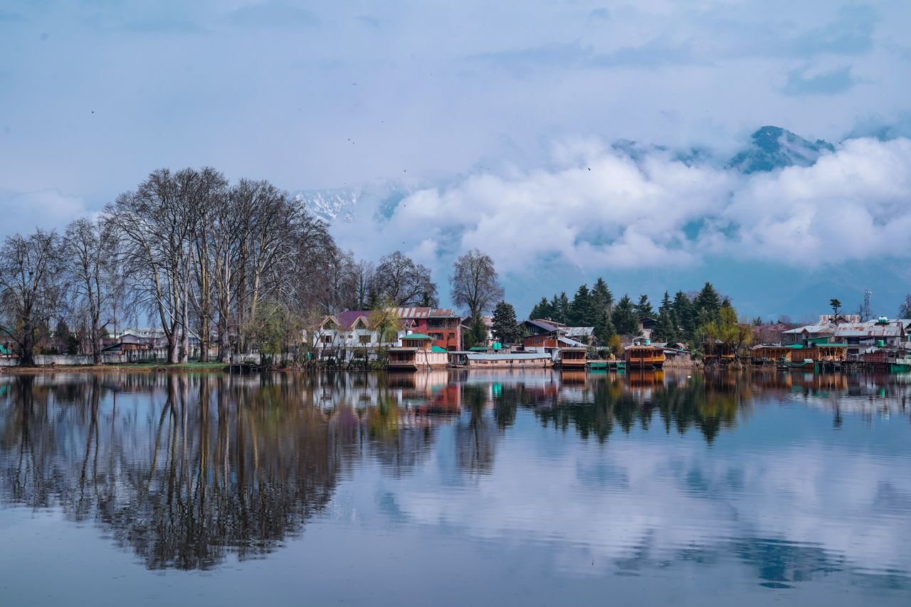 Peaceful lakeside town surrounded by foggy mountains and reflections on the still water, creating a tranquil atmosphere.