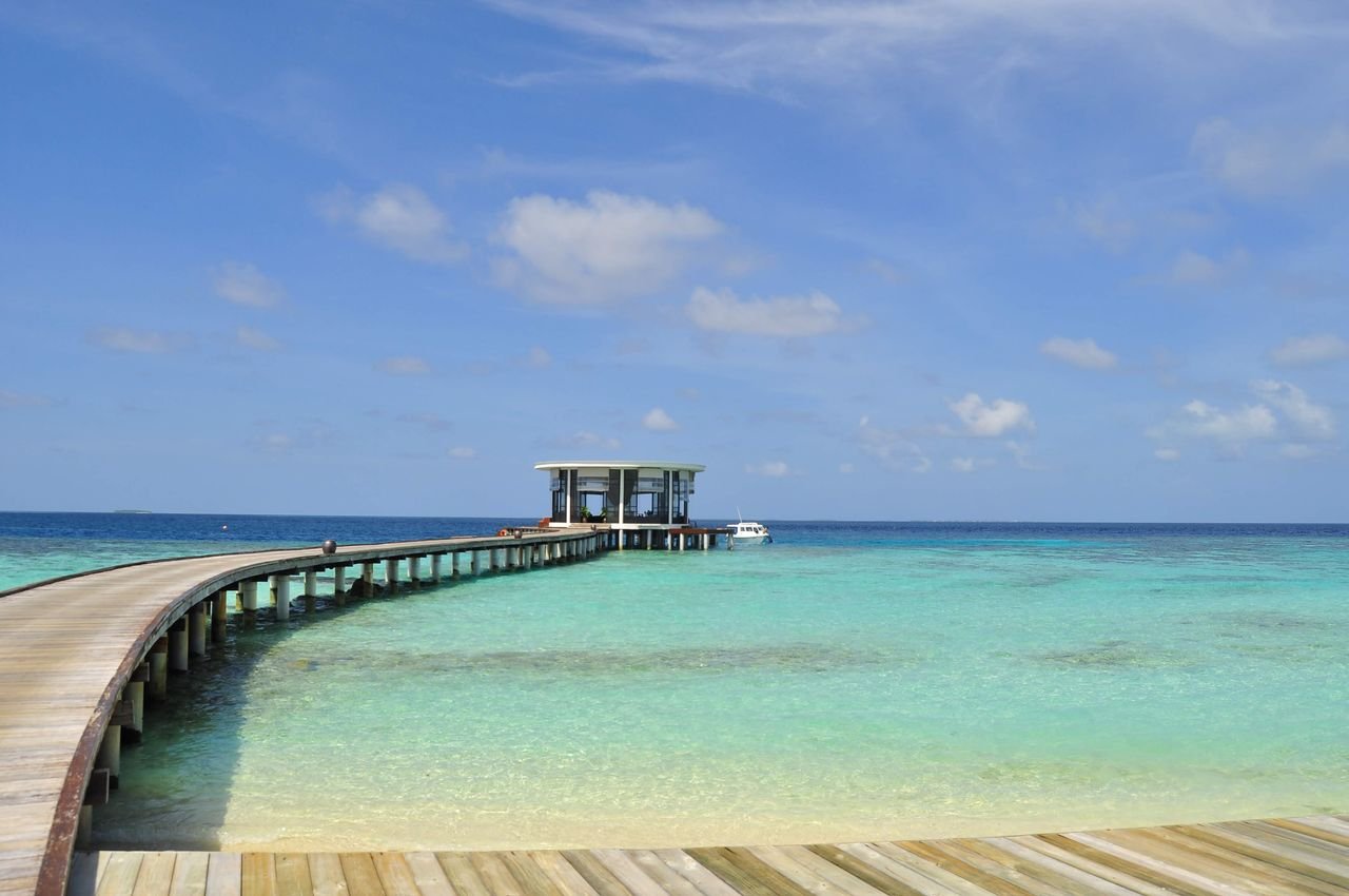 Beautiful tropical beach with a long wooden jetty stretching into the turquoise ocean in the Maldives.